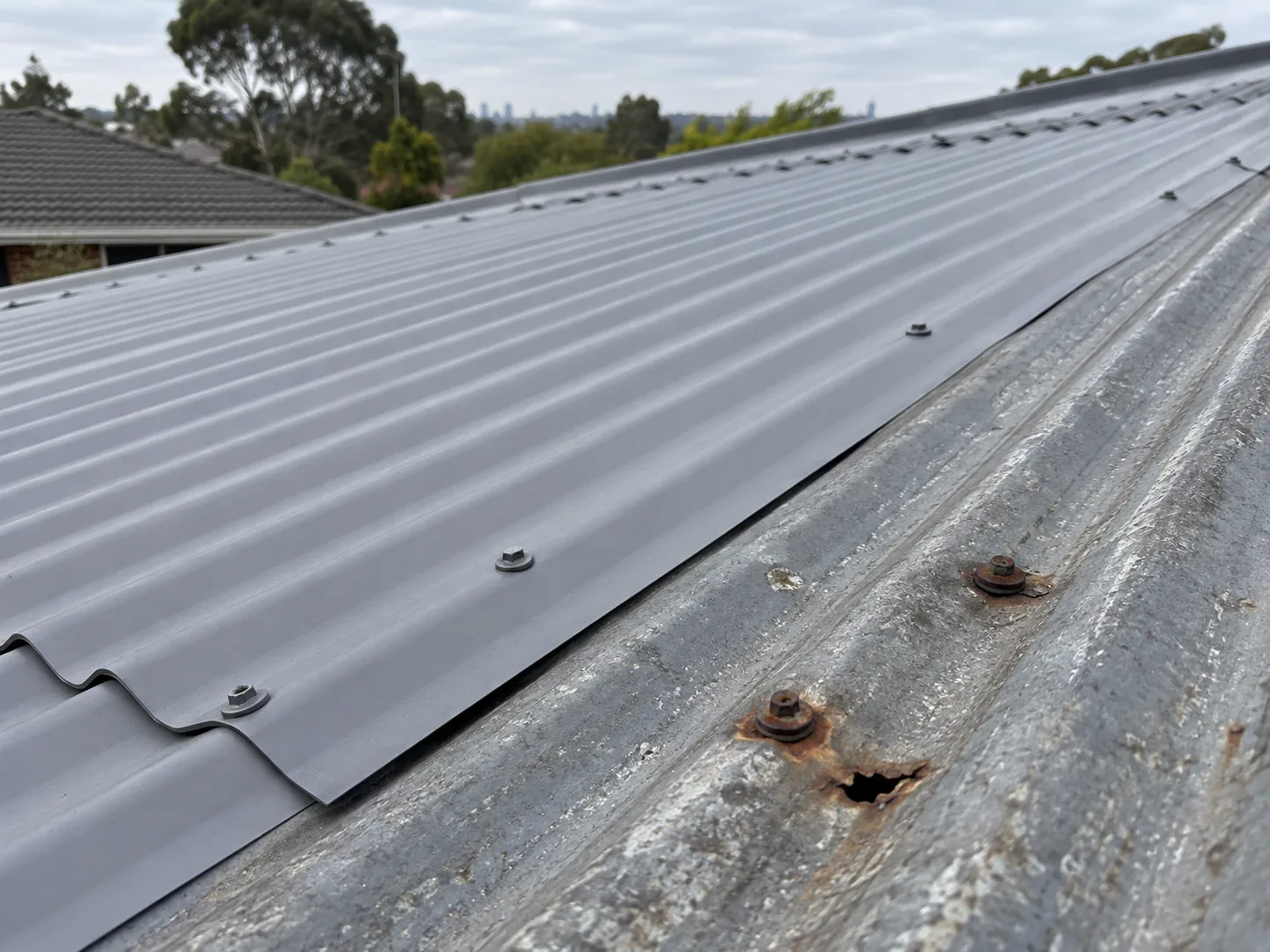 A new metal roof sheet lapped over an old rusted sheet, rust and a hole around the old screw heads