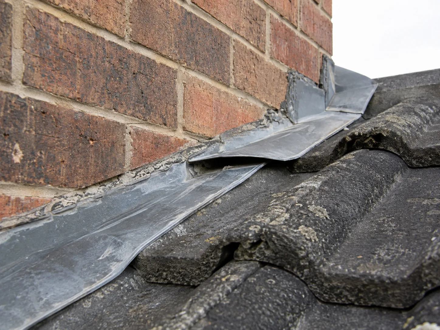 A wall flashing lifted away from the brickwork above a tile roof