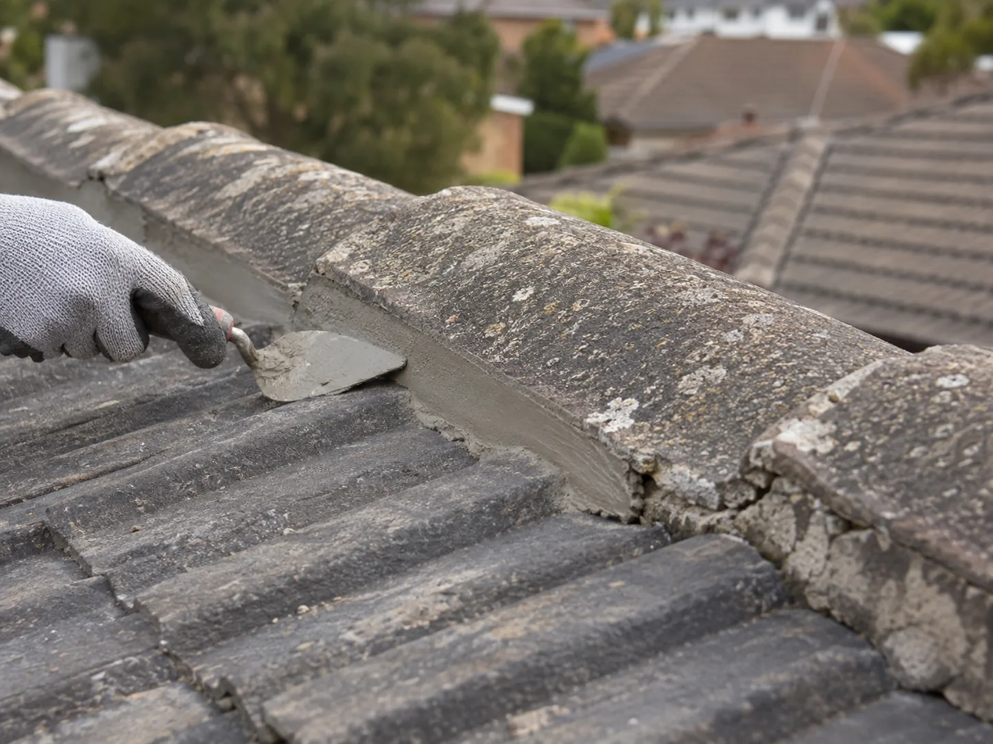 A ridge cap being rebedded, mortar worked in under the cap with a trowel