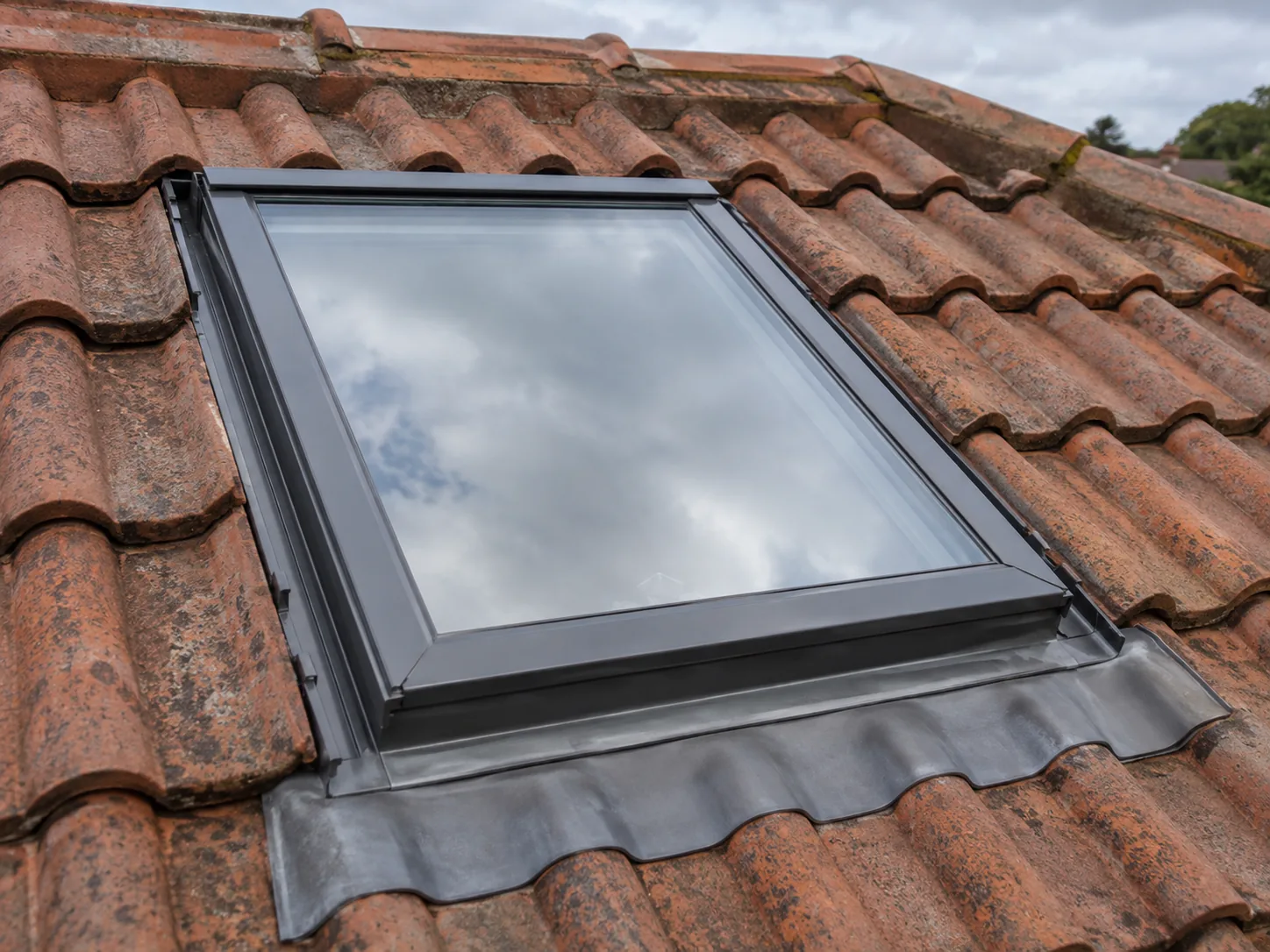 A skylight set into a terracotta tile roof with its flashing dressed over the tiles below