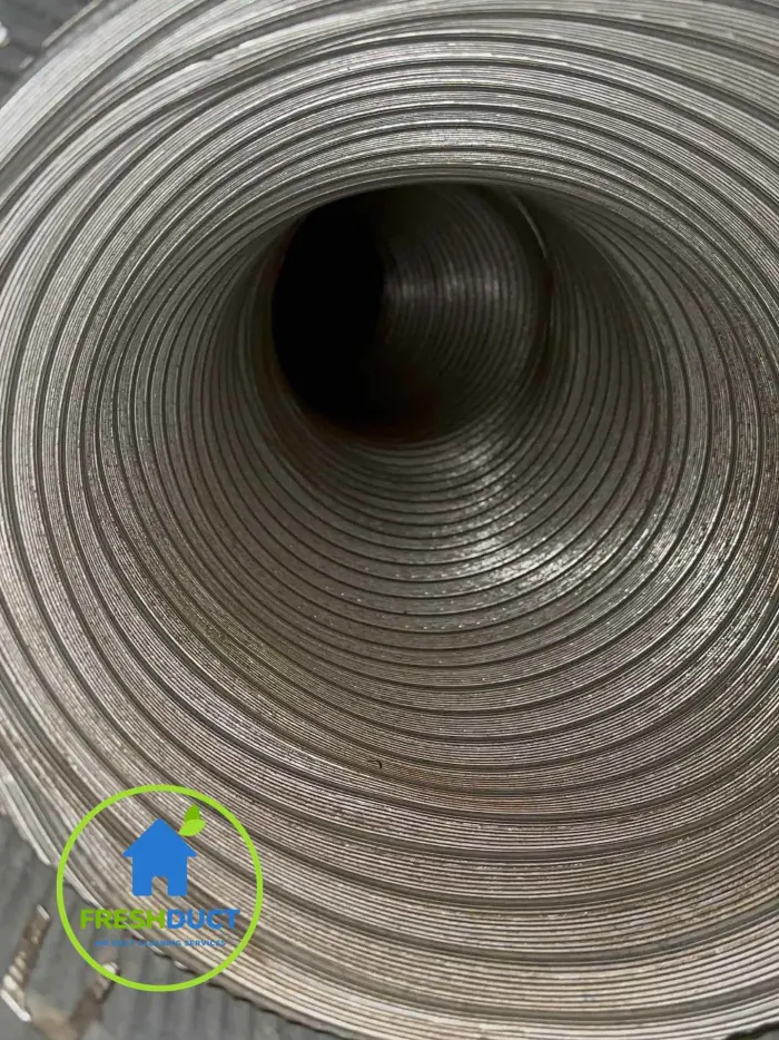 The same air duct after a FreshDuct clean, bright bare metal helix visible